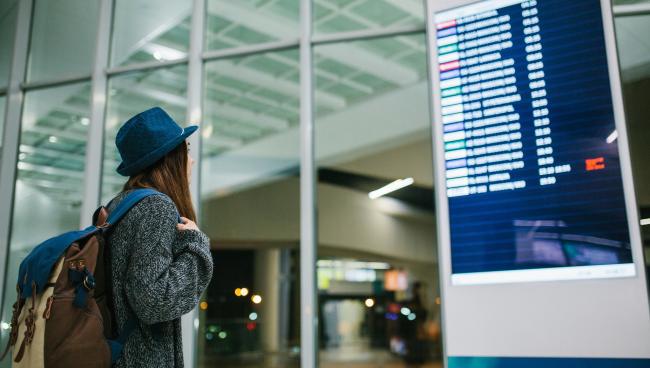 Девушка в аэропорту стоит перед таблом вылета